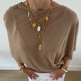 Person wearing a brown top and white pants with layered gold necklaces and bracelets.