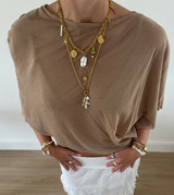 Person wearing a brown top and white pants with layered gold necklaces and bracelets.